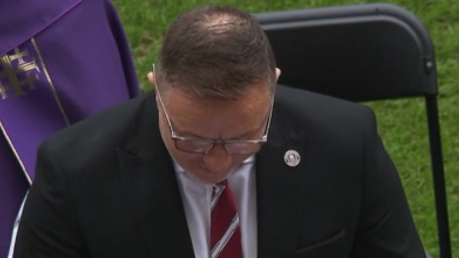 Kris Radlinski is wearing a black suit. He is looking down at his notes as he gives a speech inside the stadium.