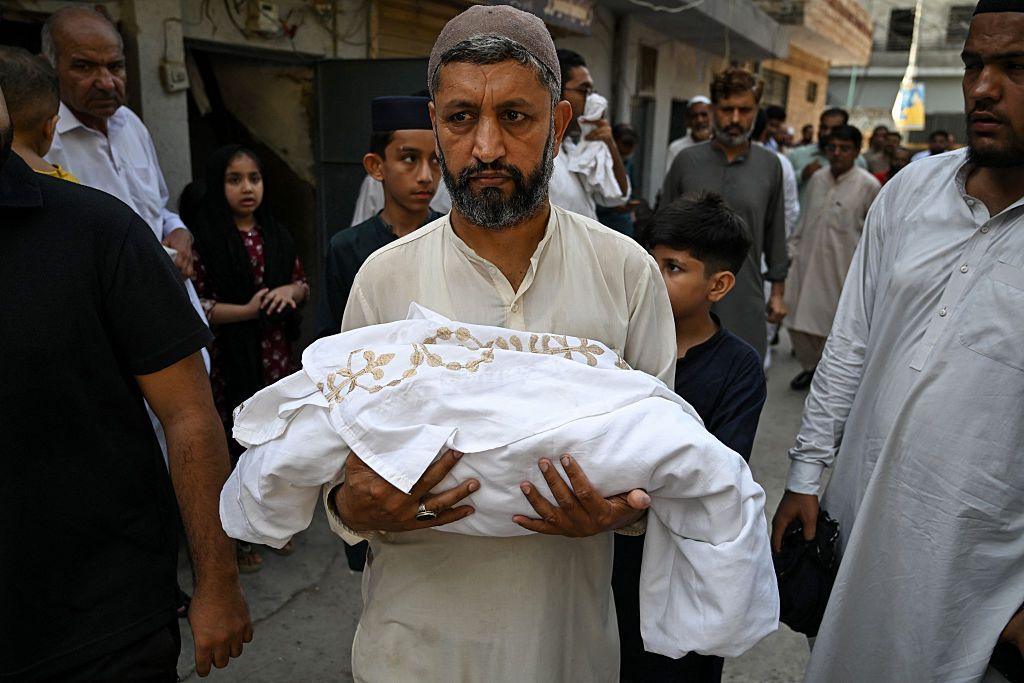 A man carries the body of a newborn child who died following a fire at the Mother and Child Health (MCH) ward of the Pakistan Institute of Medical Sciences (PIMS) Hospital, during a funeral in Rawalpindi on August 26, 2026.