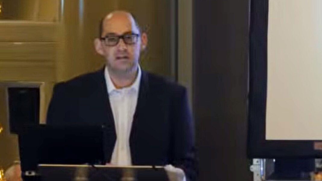 Lucy Letby ‘boyfriend’ doctor named as court order lifted Dr Mark Deakin is speaking at a podium, giving a presentation. He is balding, and wearing glasses, a blue shirt and white shirt.