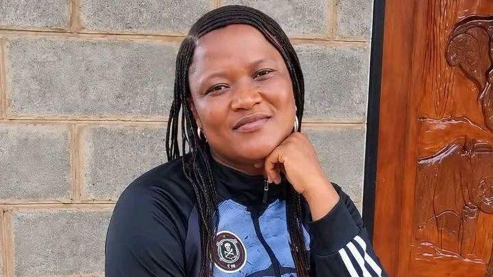 Itumeleng Kekana wears a blue tracksuit as she rests her left arm on her knee and looks at the camera.