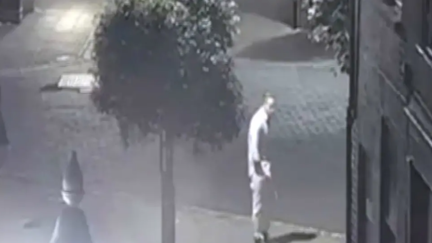 Grainy CCTV footage showing the figure of a man standing on a street next to a tree.