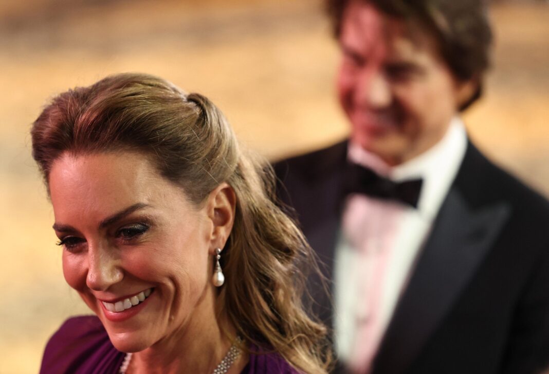 The Princess of Wales smiling with one of her earrings visible, with Tom Cruise behind her