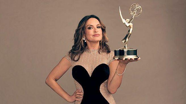 Actor Mariska Hargitay wears a black and beige dress while holding an Emmy award in one hand with her other hand on her hip