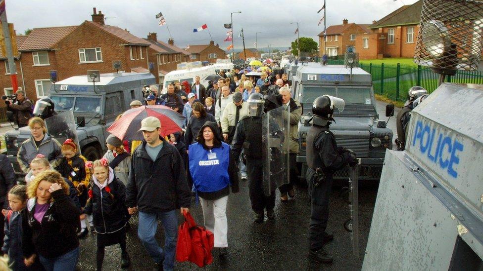 Families walk along the Ardoyne Road shielded by security forces on their way to Holy Cross Primary School in North Belfast, 7 September 2001