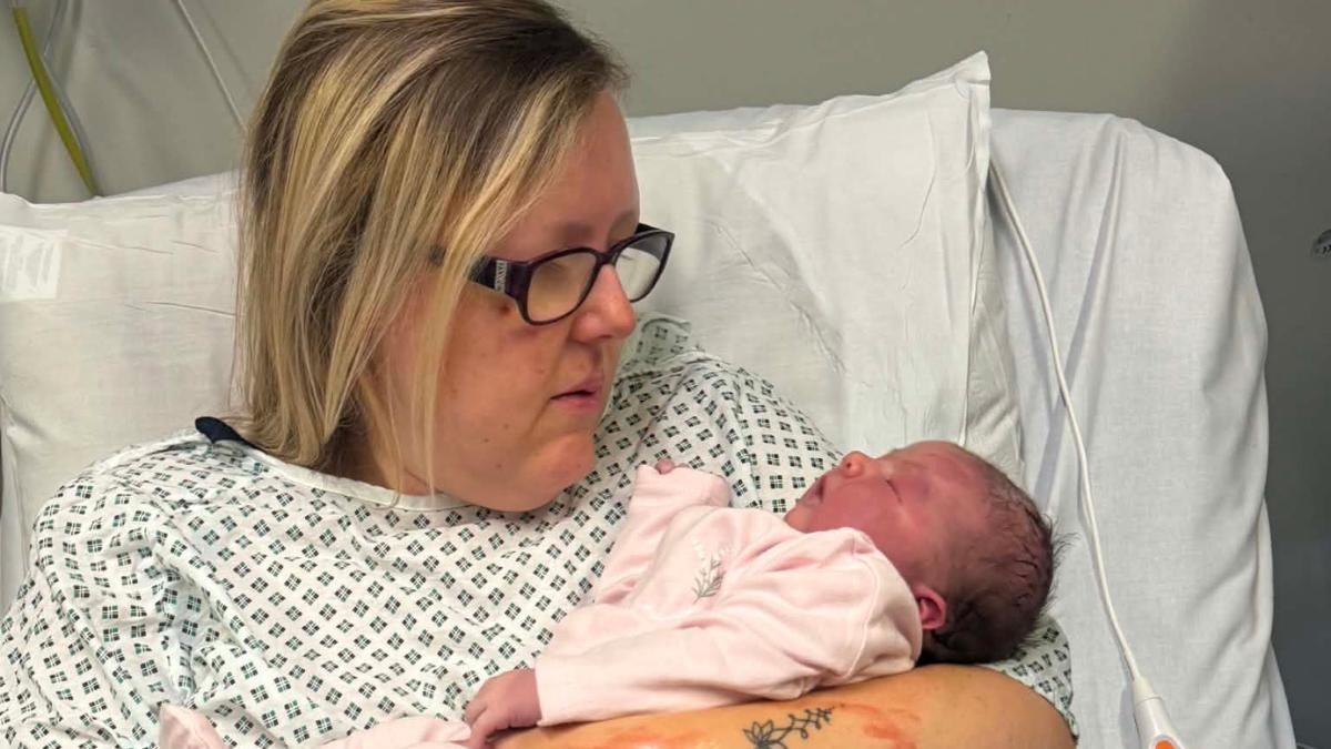 A woman with blonde hair and glasses holding a baby