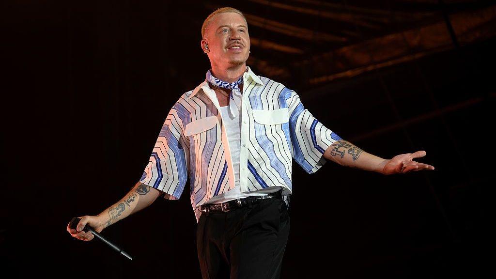 Macklemore performing on stage with microphone in hand