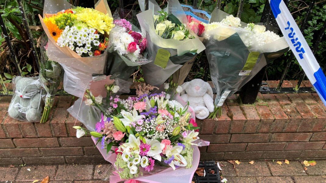Four in court over murder of baby stabbed to death Several bouquets of flowers in plastic wrap propped against a low wall topped with metal railings. A toy bear and a tow rabbit have also been placed on the wall. In the top right corner of the photo a section of blue and white police tape can be seen.
