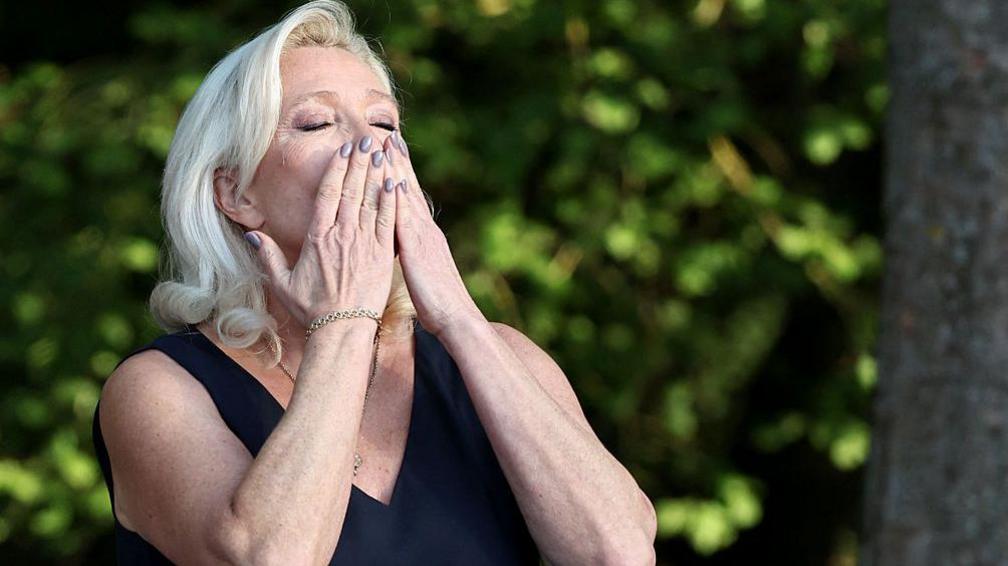 President of Rassemblement National parliamentary group Marine Le Pen reacts as she addresses the audience during a RN party event