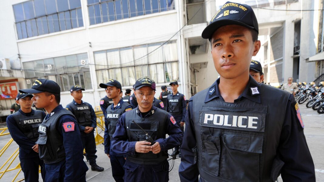 A group of Thai police officers in navy uniform with the word Police on their vests. They wear navy caps with yellow writing on.