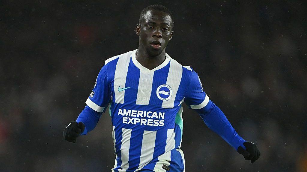 Yankuba Minteh, wearing Brighton's blue-and-white-striped kit, runs during a Premier League match