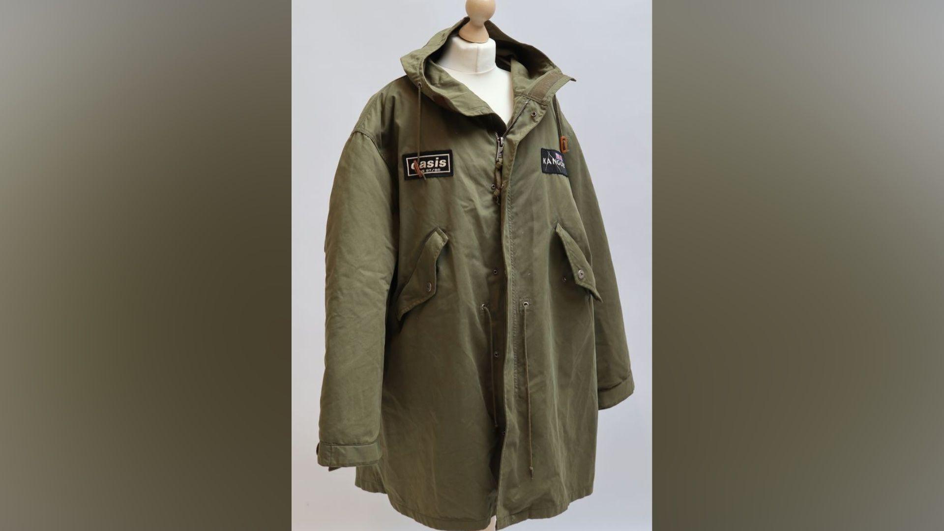 A green parker coat with a black Oasis badge is perched on a manikin in front of a white background.