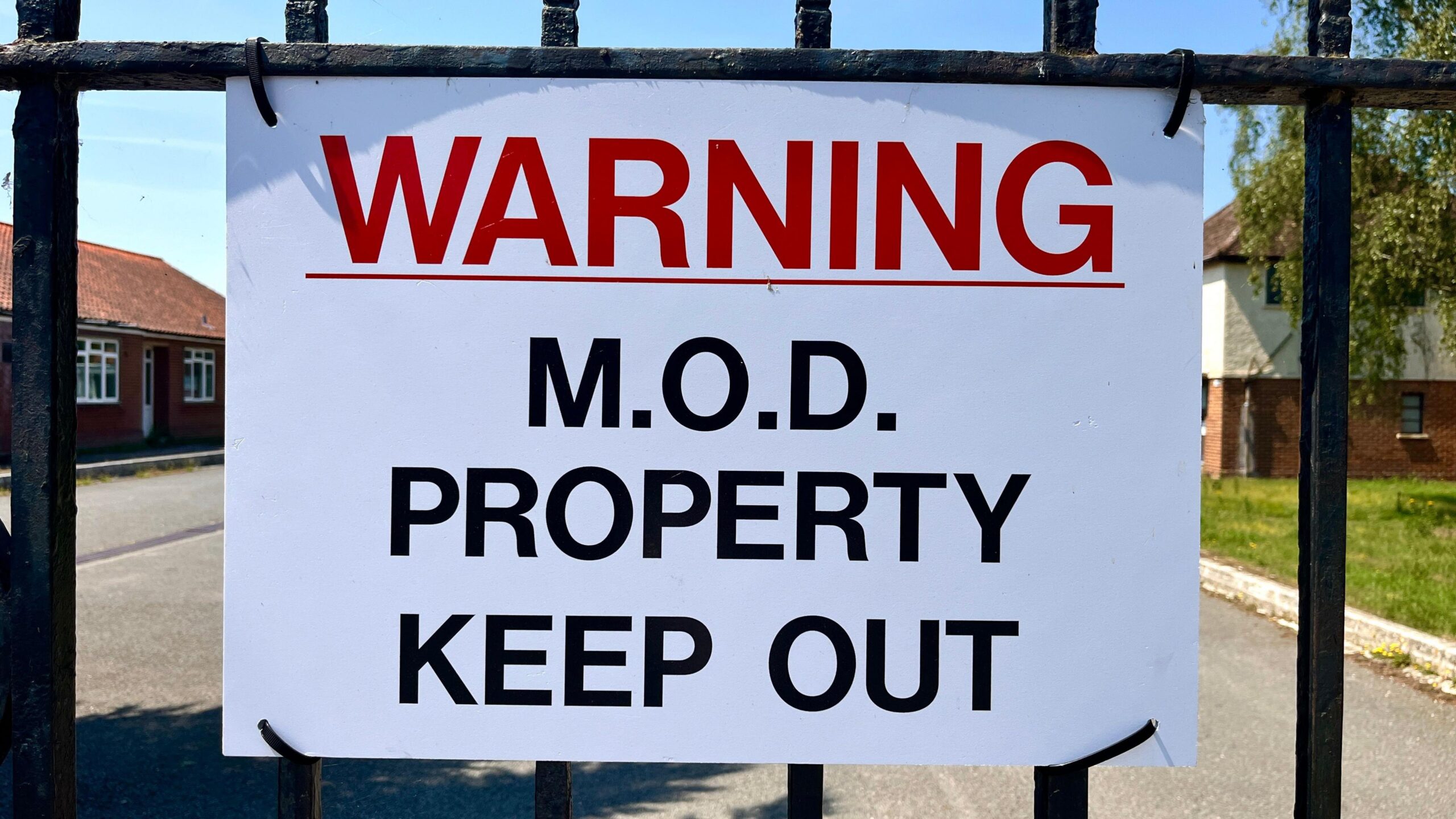 A sign says: "WARNING: MOD PROPERTY KEEP OUT." It is white, with red and black printing and is hung on a metal gate.