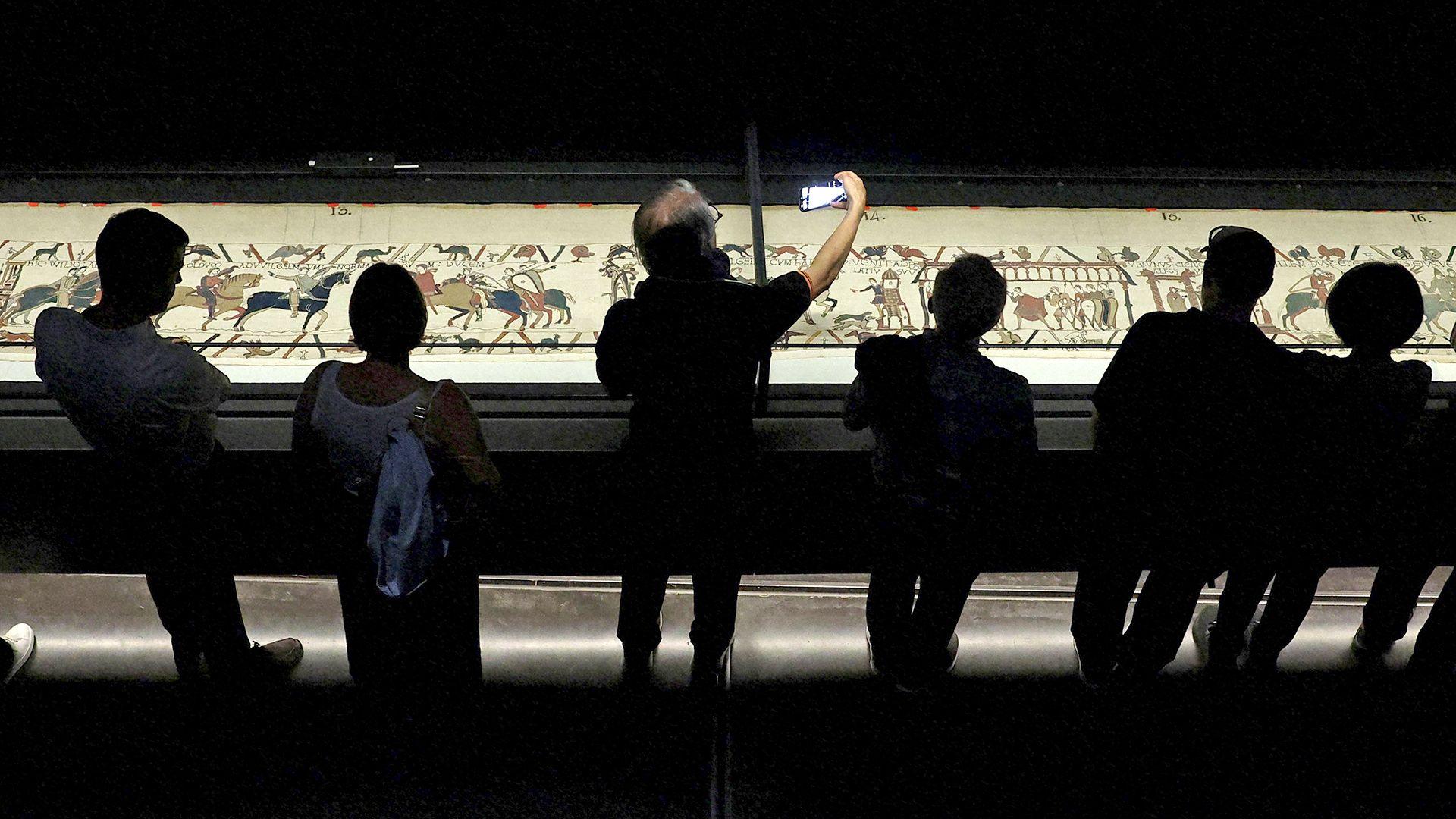 Visitors view an illuminated Bayeux Tapestry as it is displayed in a darkened exhibition room at the British Museum in London.