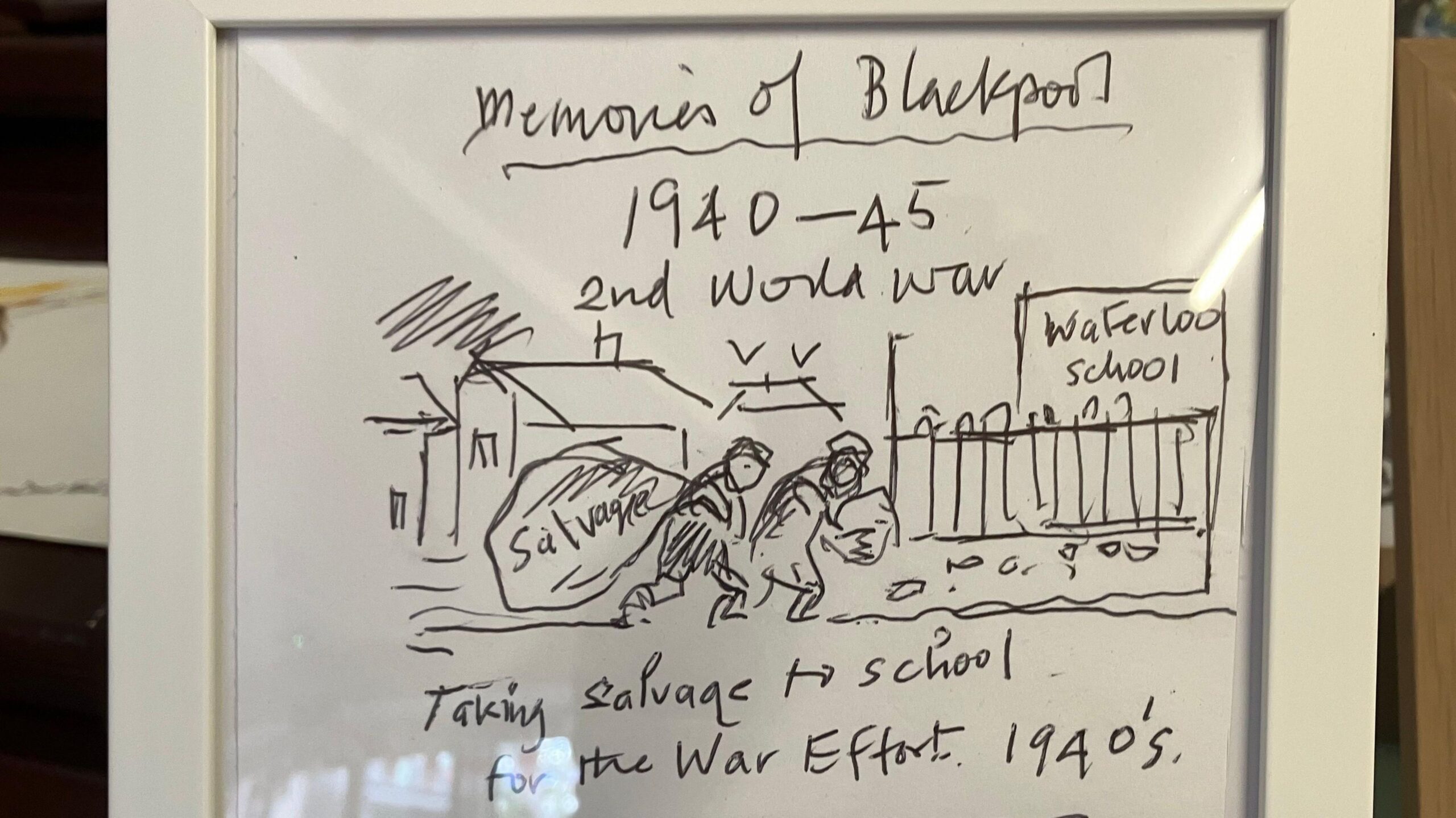 A close-up photograph of a framed hand-drawn sketch and handwritten memoir displayed behind glass. The drawing includes several handwritten captions: “Memories of Blackpool”, “1940-45”, “2nd World War”.