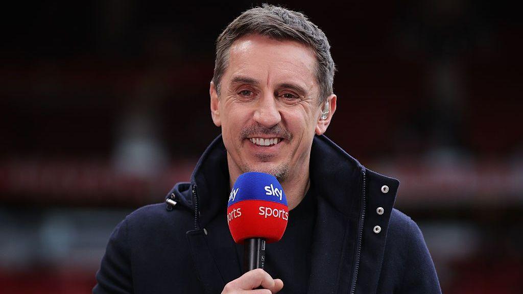 Gary Neville smiling and holding a Sky Sports microphone