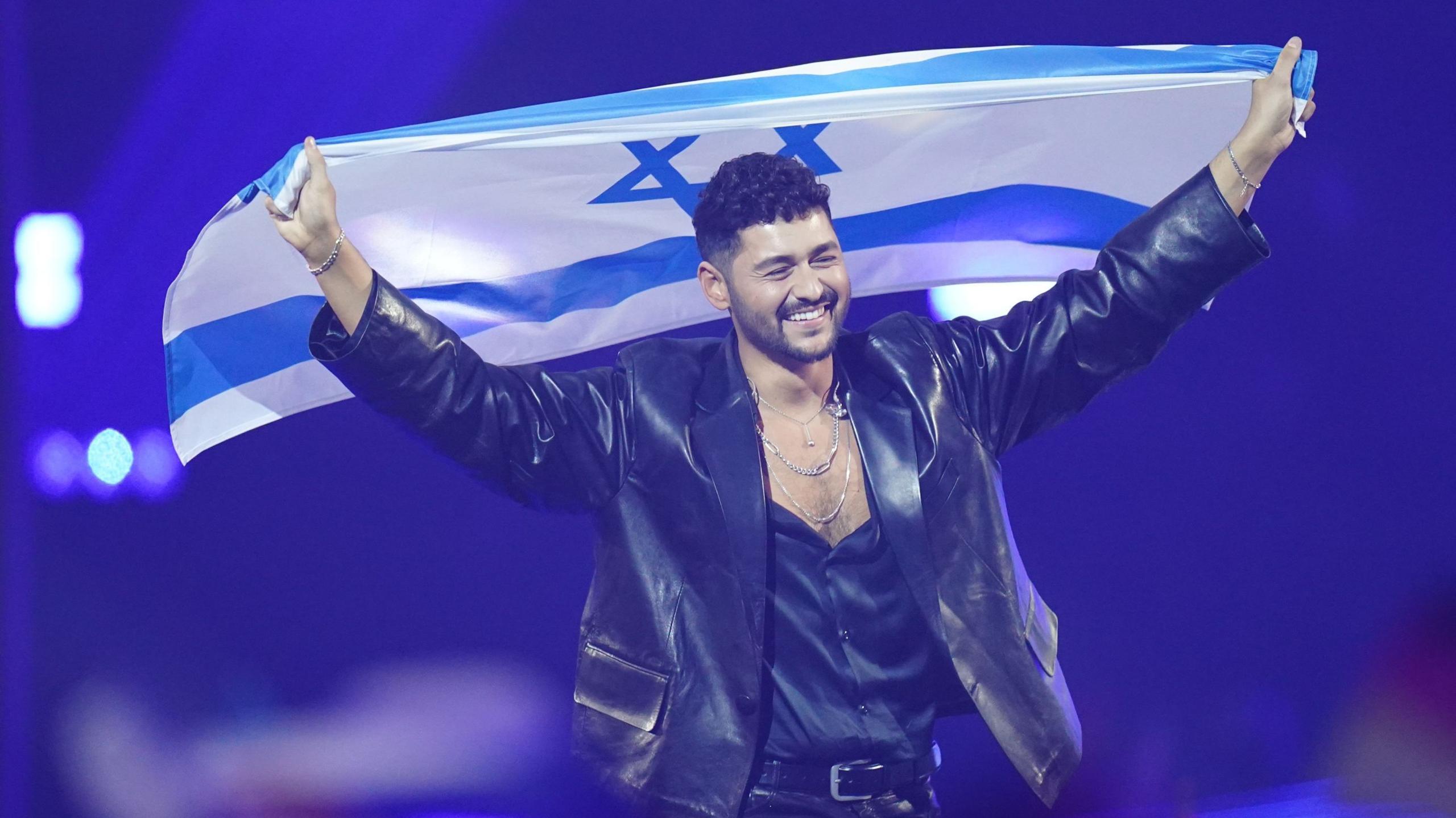 Noam Bettan representing Israel, during the grand final for the Eurovision Song Contest in the Wiener Stadthalle in Vienna, Austria. He is wearing dark leather clothing holding up an Israeli flag
