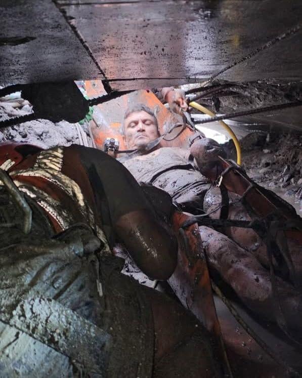 A man covered in mud on an orange stretcher is pulled through a tiny passageway