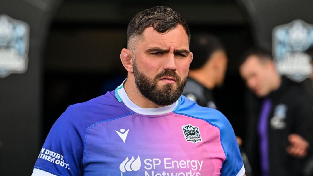Jamie Bhatti walks out of the tunnel onto the pitch, he is wearing a purple and pink faded gradient shirt with Glasgow Warriors branding