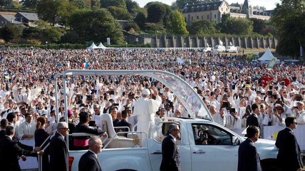 The pope in the popemobile waving to a crowd of worshipers at Lourdes