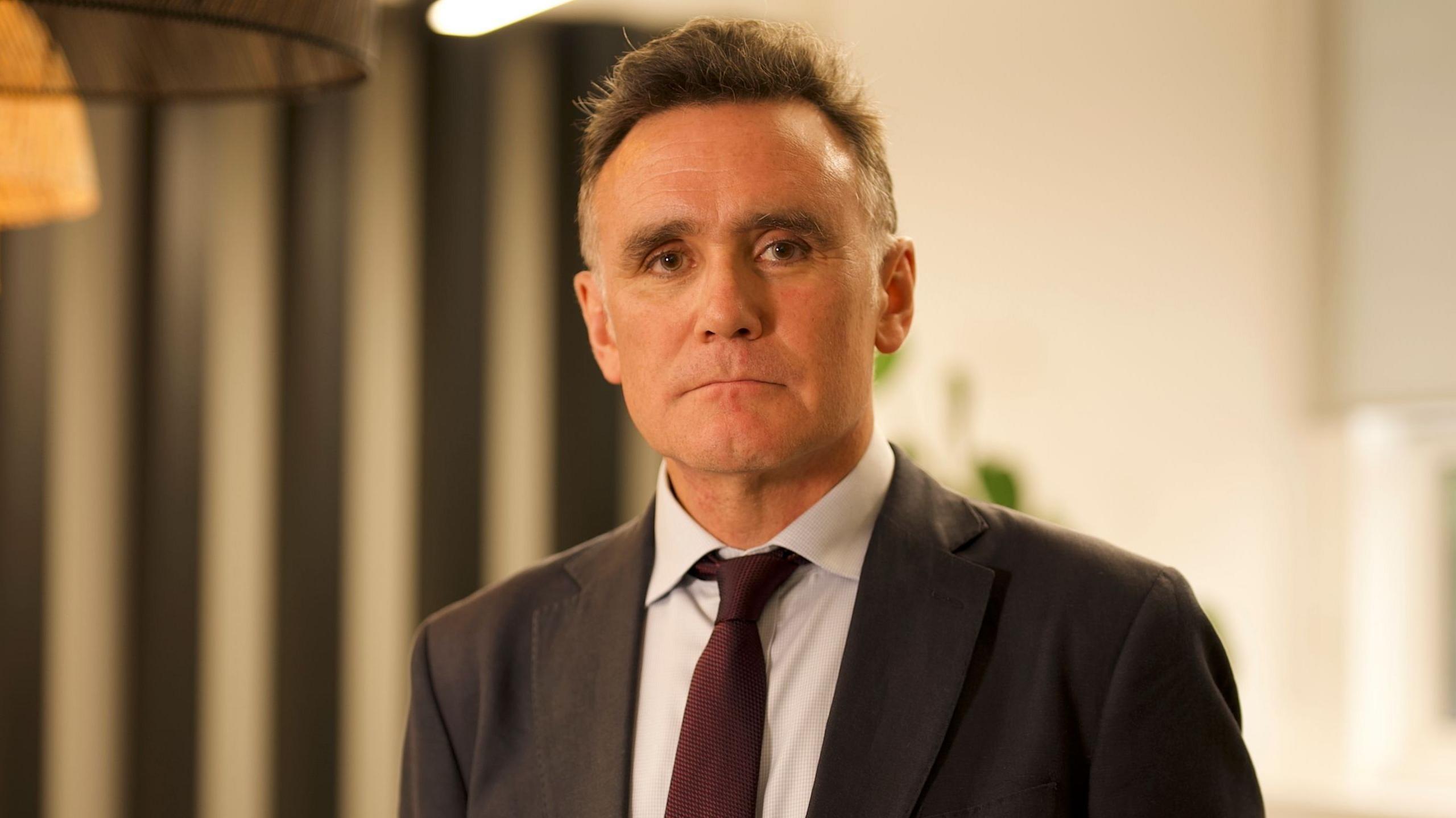 Headshot of middle-aged man with short brown/grey hair and brown eyes in a suit