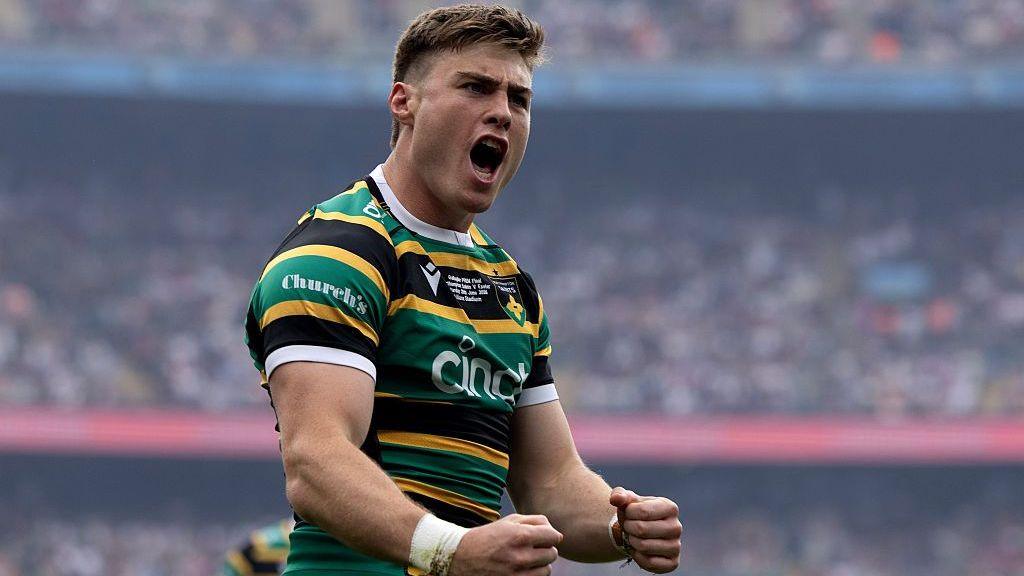 Tommy Freeman puts both clenched fists out ahead of him in celebration, yelling to the crowd, wearing Northampton Saints Green, gold and black home kit