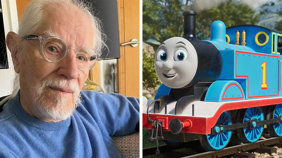 A composite image, with Christopher Awdry on the left in a blue jumper. He is wearing glasses and is looking directly into the camera as he sits on a sofa in a living room. On the right is a still from the Thomas the Tank Engine animation. Thomas is a bright blue locomotive with the number 1 on his side. There are tracks on the ground leading left to right and there are animated trees in the background