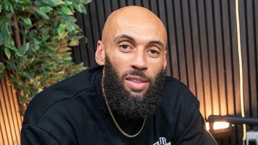 Aaron Dale, who is bald with a black beard and wearing a black sweatshirt and gold chain looks at the camera.