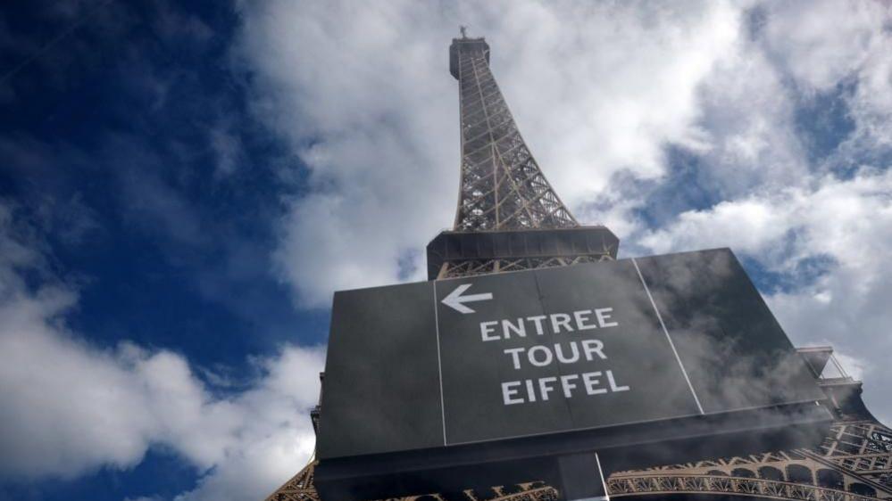 The Eiffel Tower is seen from the base of the monument with clouds and blue skies around it