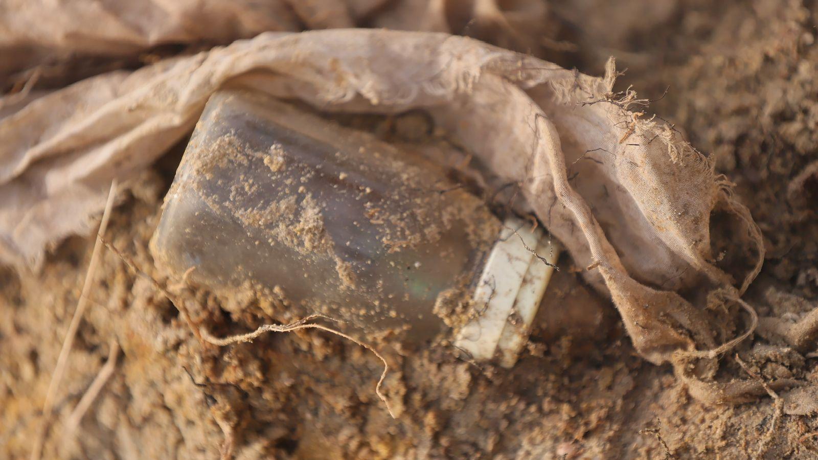 A baby's bottle is partially covered in dirt at the grave site.