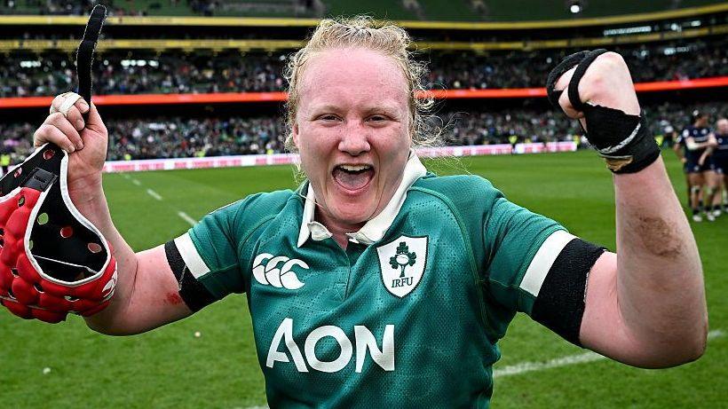 Aoife Wafer celebrates at the side of the pitch with both arms raised and a happy expression on her face, as she wears Ireland's largely green match shirt