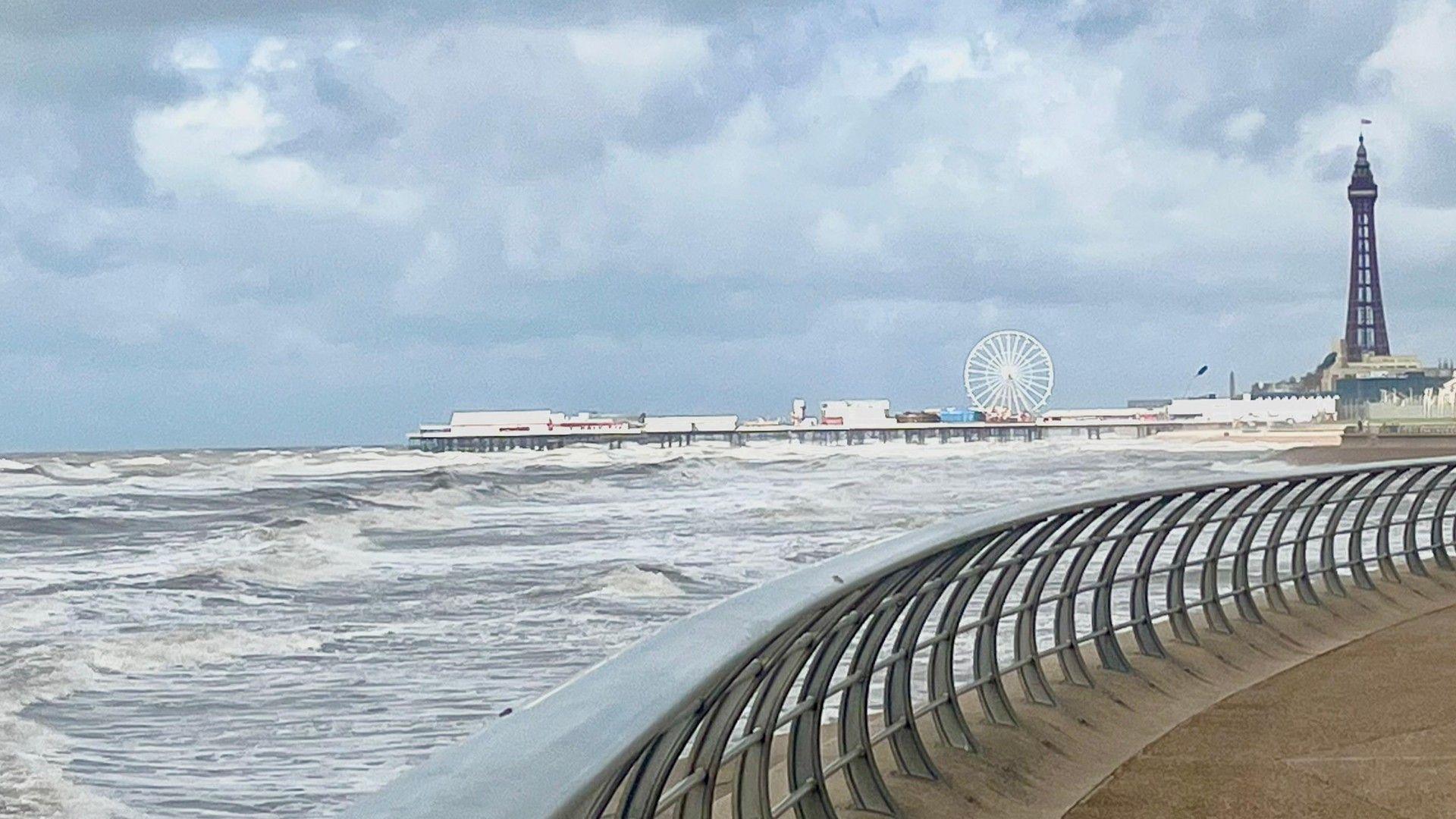 Coastline in Blackpool with the Blackpool Tower in shot and a pier stretching out into a choppy sea.