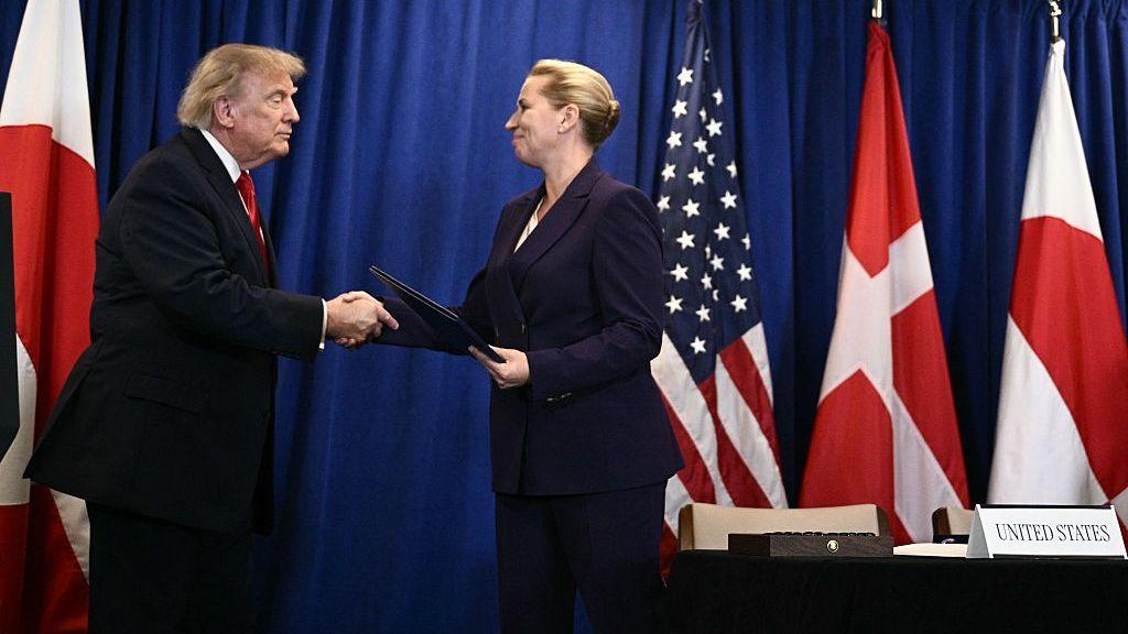 Trump on left and Frederiksen on right, both in dark-colored suits in front of row of flags and blue background