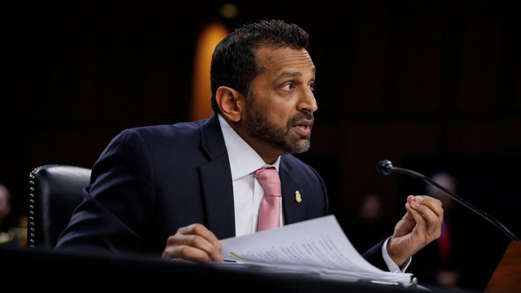 Kash Patel, wearing a navy suit and pink patterned tie, speaks into a microphone at a Senate hearing.