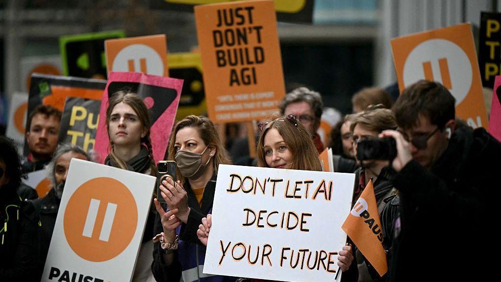 A group of campaigners at a protest in London in February. A woman holds up a sign which reads "Don't led AI decide your future". Behind her, another sign reads "Just don't build AGI".