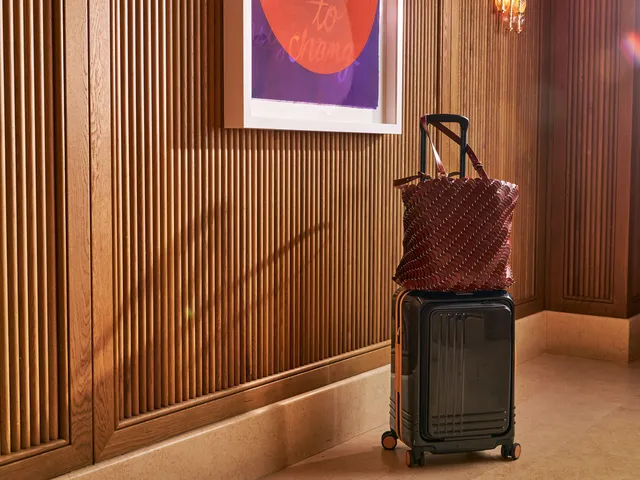 A black suitcase with a leather bag resting on top in a hotel hallway