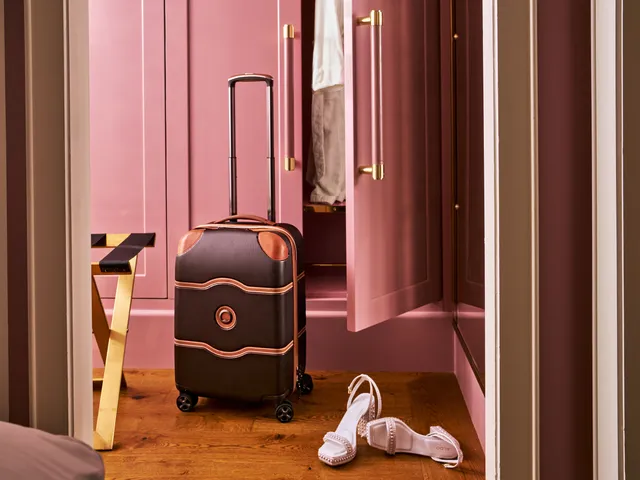 A suitcase next to an open closet door and a pair of light pink heels