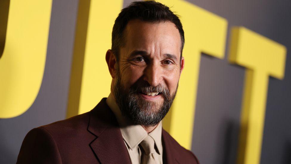 Noah Wyle at The Pitt Los Angeles premiere, wearing a brown suit and beige shirt and tie