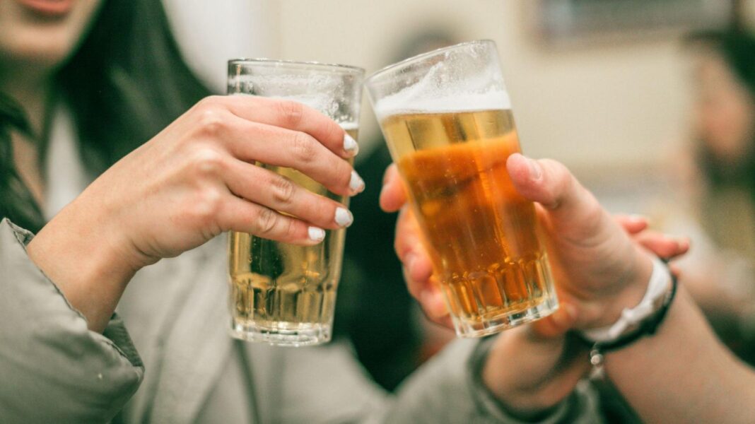 A pair of beer-filled glasses being knocked together in a bar setting.