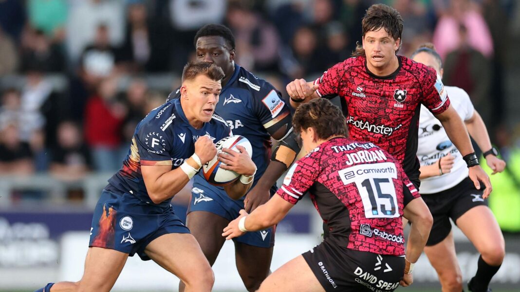 Joe Carpenter (left) of Sale runs towards Bristol's Tom Jordan (JORDAN 15) with other players from each side watching on