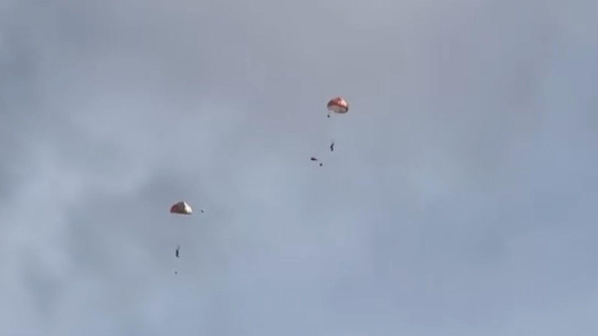 Two figures floating in the sky with parachutes