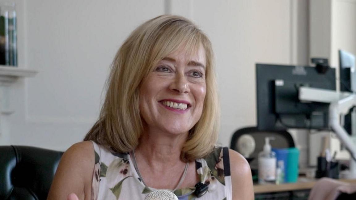 Prof Jane Harrington, a woman with shoulder length blonde hair, sitting in an office, smiling towards the camera.