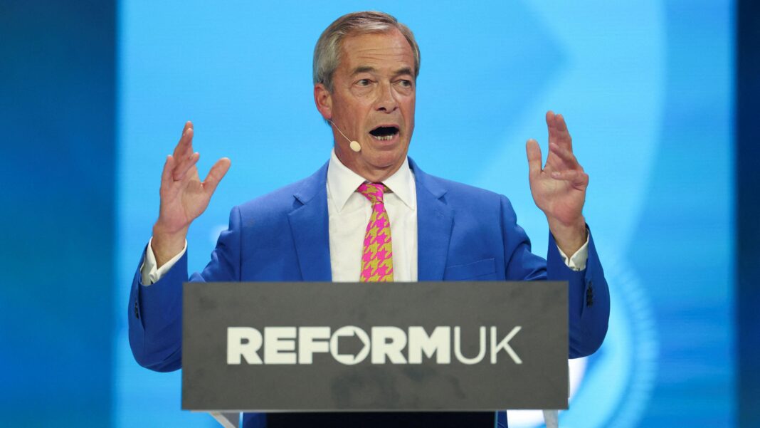 Nigel Farage holds up his hands as he gives his conference speech from behind a podium with Reform UK's logo.