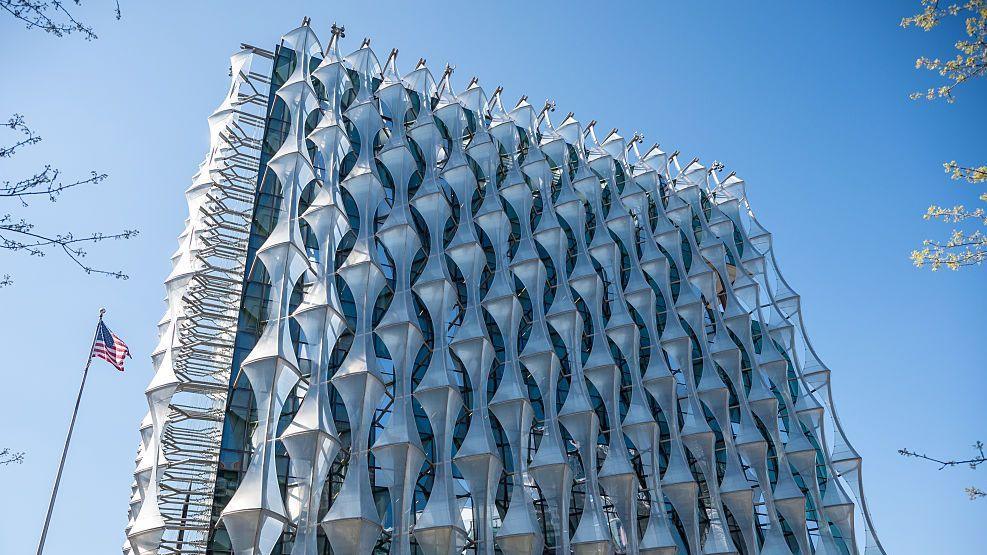 A building that looks like a silver metal cube with crystal style metal decoration covering it entirely. A US flag can be seen flying on a pole to its left.