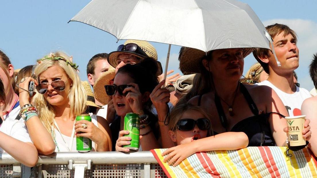 People standing in a crowd wearing sunglasses and holding a silver umbrella.