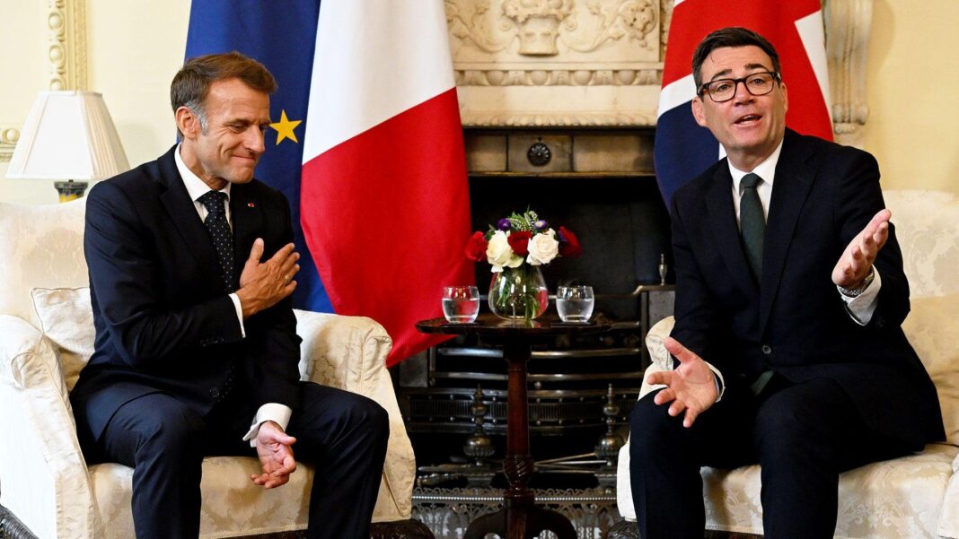 Emmanuel Macron and Andy Burnham sit on chairs in Downing Street smiling and in conversation with their respective flags behind them.