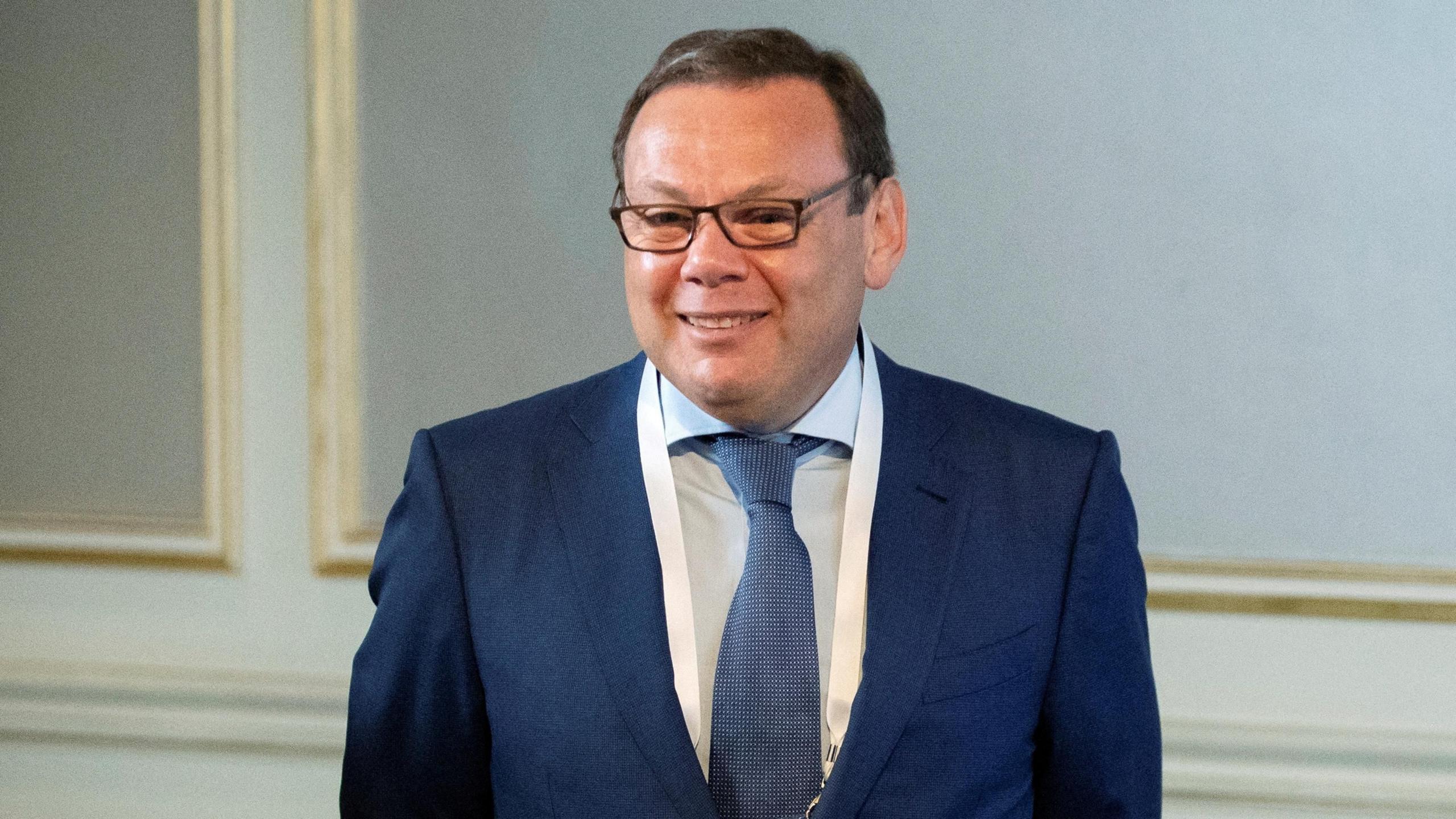 Mikhail Fridman, a middle-aged man wearing a dark suit and glasses, smiles at the camera