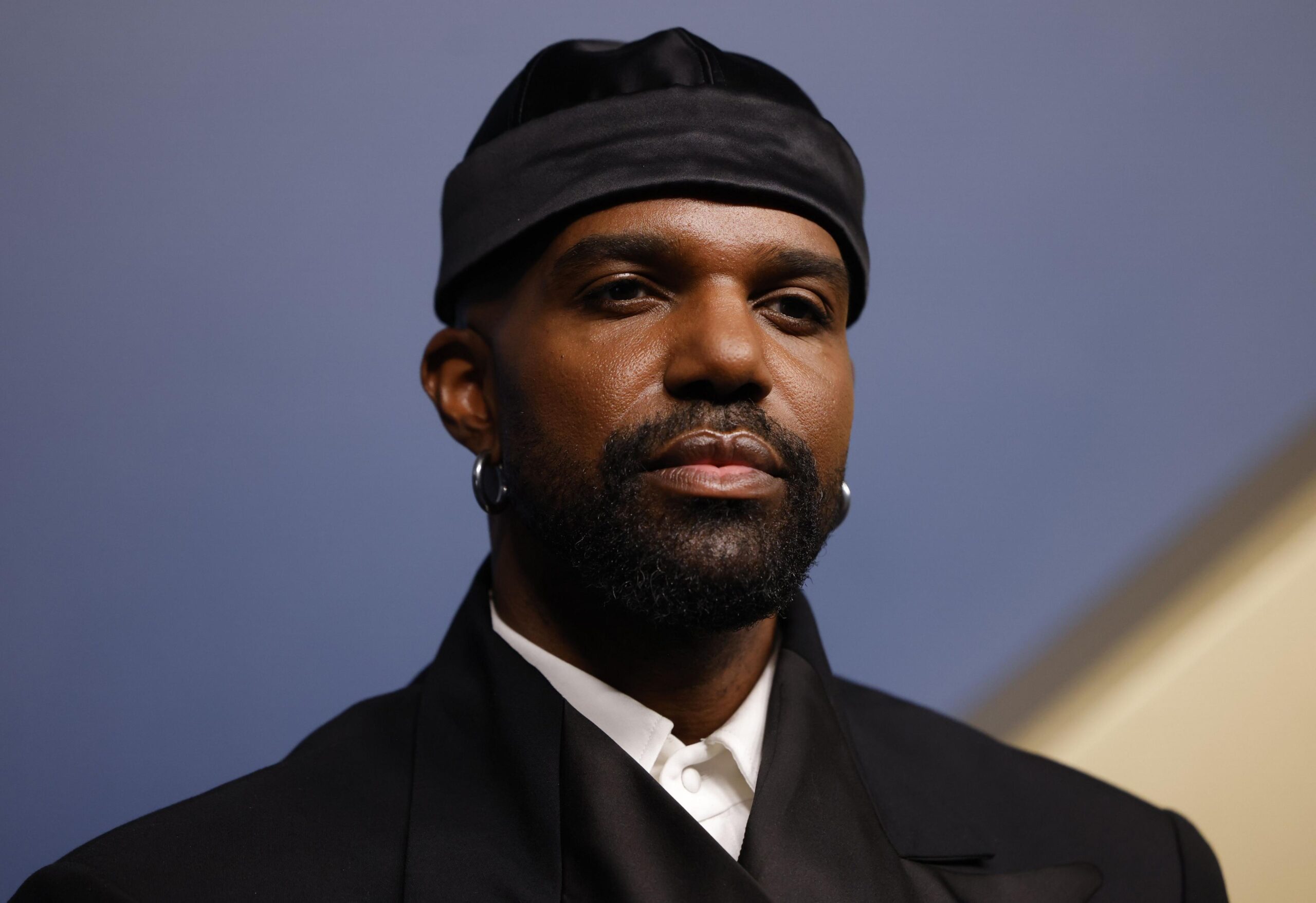 Carl Clemons-Hopkins in a black jacket, white shirt and black hat