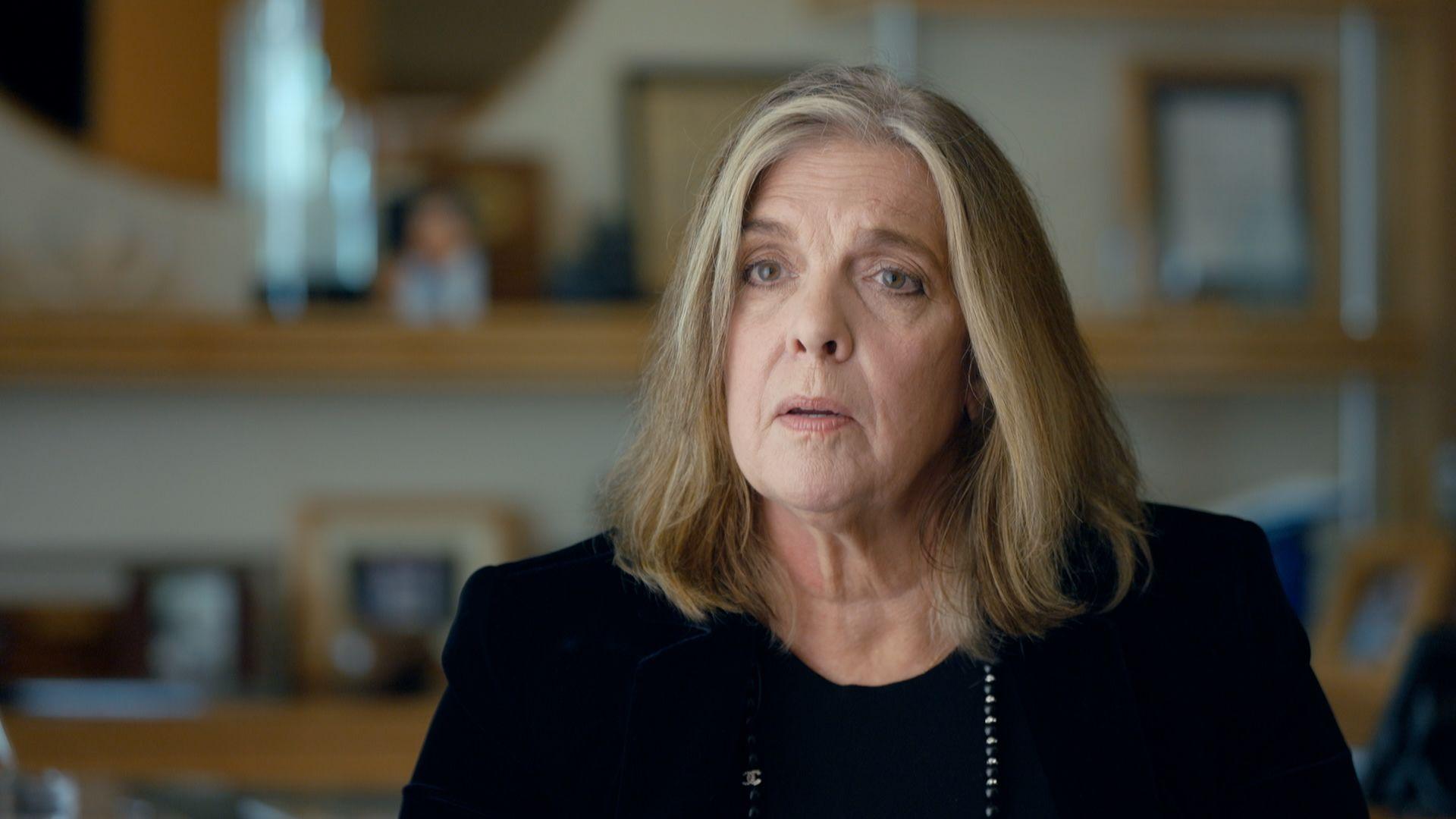 Jodi Westbook Flowers, a woman with shoulder-length blonde hair, wearing a dark jacket and top, speaking in her legal offices in Charleston, South Carolina. In the blurred background behind her there appear to be framed certificates and photographs on the shelves