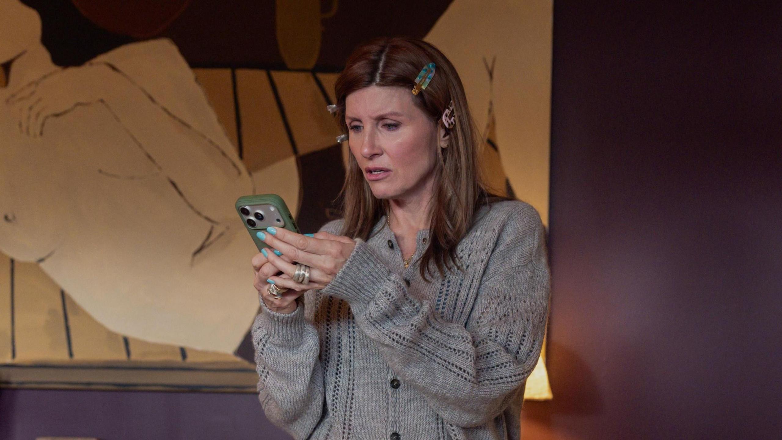 Sharon Horgan as Alex, wearing a grey cardigan, and looking at her mobile phone