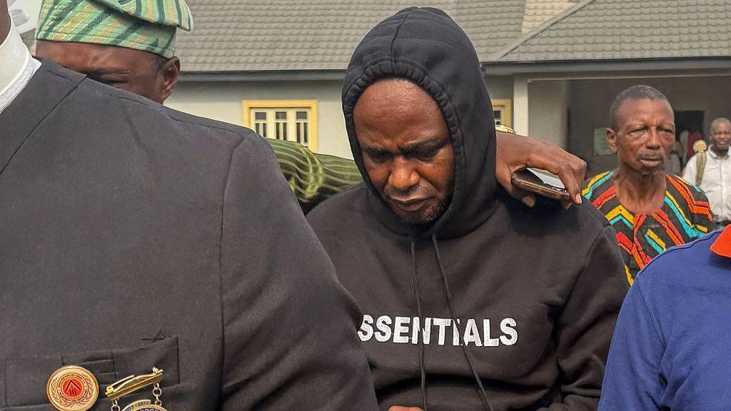 Adeniyi Mobolaji Kayode is in a black hoody with his head bowed as someone has their arm round him as he is led from court in a picture taken in January 20 this year